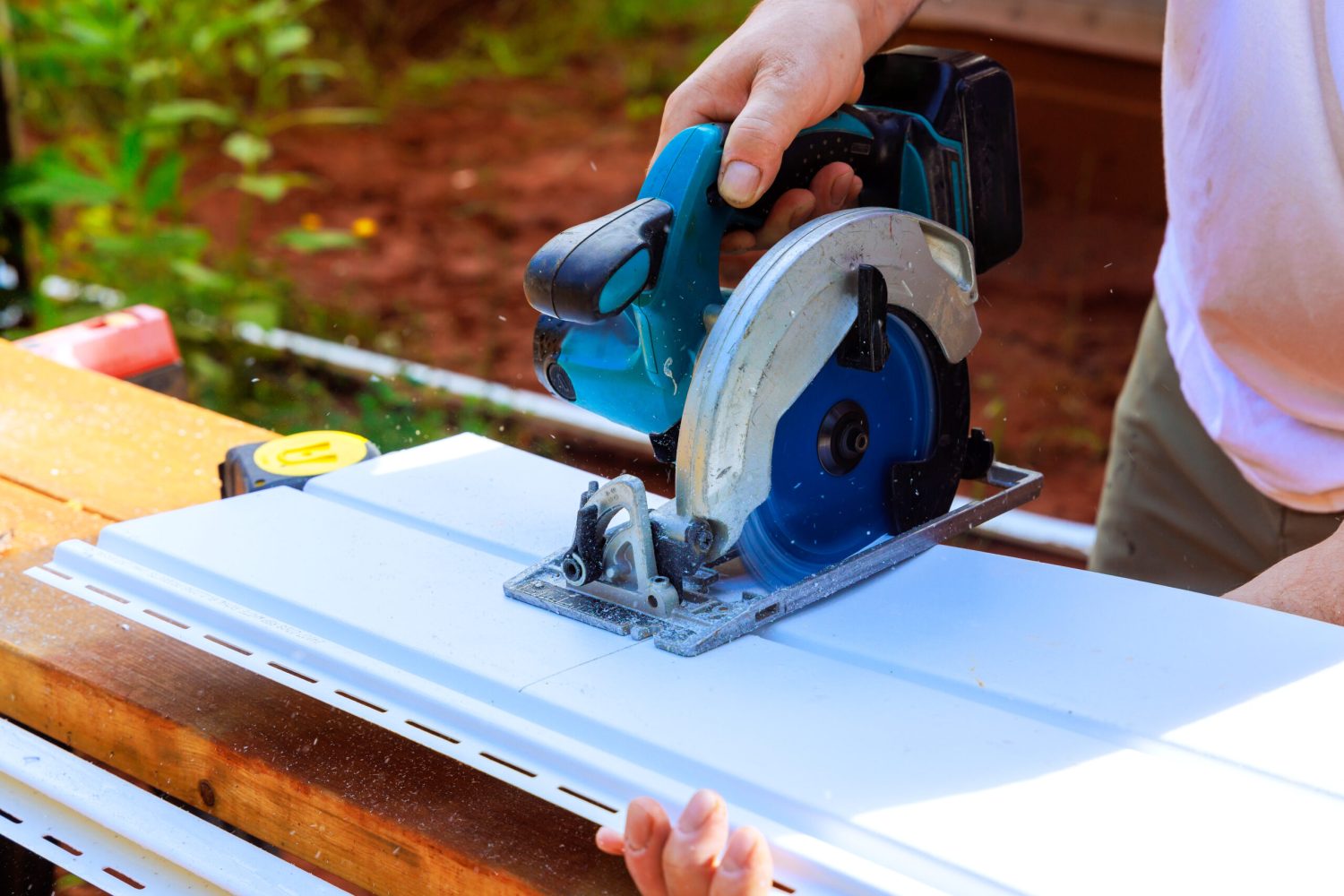 Using circular handsaw, worker cuts plastic vinyl siding to size prior to installation